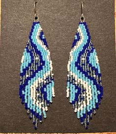 two pairs of blue and white beaded earrings on top of a gray surface with a black background