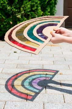 a person holding an umbrella made out of colored paper on the sidewalk with trees in the background