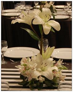 there is a vase with flowers in it on the dining table set for an event