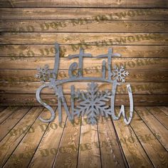 a metal sign that says let it snow on top of a wooden floor with snowflakes