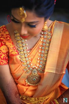 a woman wearing an orange and gold sari with pearls on her neck, necklaces and