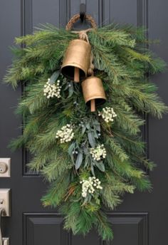 a christmas wreath hanging on the front door with bells and greenery attached to it