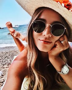 a woman wearing sunglasses and a straw hat on the beach with her hand under her chin