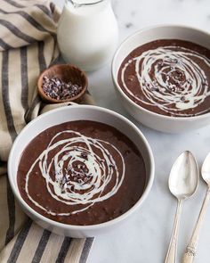 two bowls filled with chocolate pudding next to a bottle of milk and spoons on a table