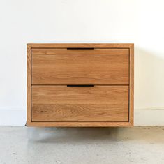 a wooden dresser sitting on top of a cement floor next to a white wall with two black handles