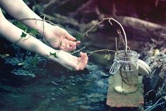 two hands reaching for something in a jar on top of the ground next to water