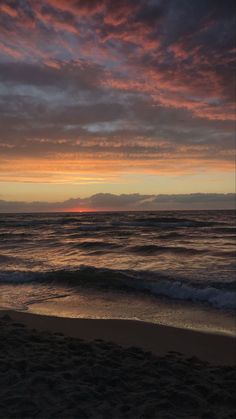 the sun is setting over the ocean with clouds in the sky and waves on the beach