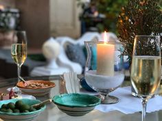 a table topped with plates and bowls filled with food next to two glasses of wine