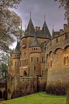 an old castle with turrets and towers on the top floor is surrounded by trees in front of a cloudy sky