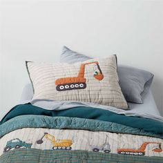 a bed topped with pillows and a quilted comforter covered in construction themed sheets