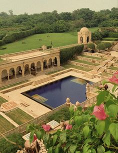 an aerial view of a large pool surrounded by greenery and stone buildings with pink flowers in the foreground