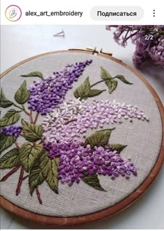 an embroidery project with purple flowers and leaves on the hoop, next to some lilacs