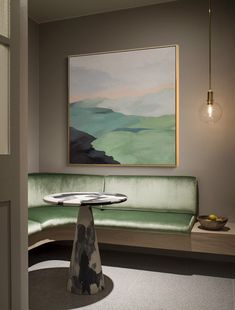 a painting hangs on the wall next to a green couch and table with a bowl of fruit