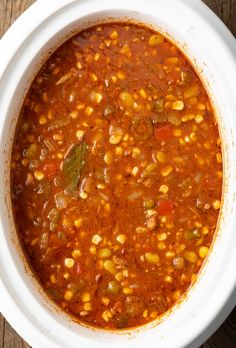 a white bowl filled with chili and corn on top of a wooden table next to a spoon