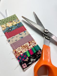 a pair of scissors next to a patchwork piece of fabric on a white surface