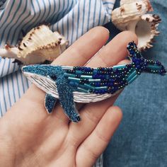 a person holding a blue and white beaded whale brooch in their left hand