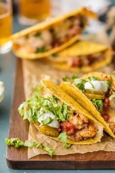 three tacos are sitting on a cutting board next to some beer and other food