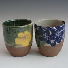 two cups with flowers painted on them sitting next to each other