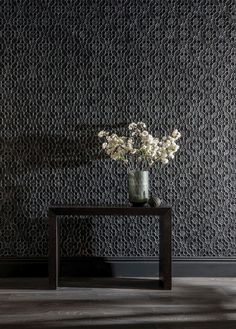 a vase filled with white flowers sitting on top of a wooden table next to a wall