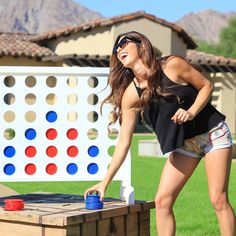 a woman in shorts playing with a giant connect - a - box game on the lawn