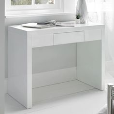 a white desk sitting in front of a window next to a vase with flowers on it