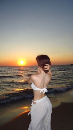 a woman standing on top of a sandy beach next to the ocean at sun set