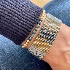 a close up of a person's arm wearing beaded bracelets and jeans