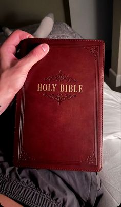 a hand holding a red bible in front of a bed