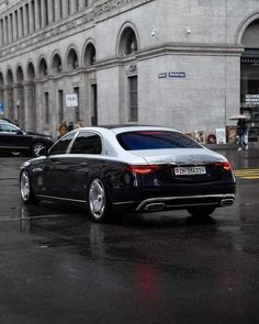 a black car parked in front of a tall building on a wet street with people walking by