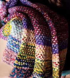 a woman is holding a multicolored knitted blanket