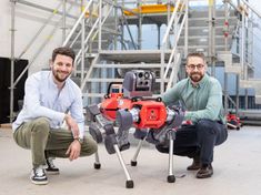 two men sitting next to each other in front of a machine that is being worked on