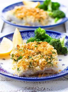 two blue and white plates with fish, broccoli and lemon wedges on them