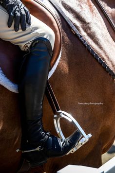 a woman riding on the back of a brown horse wearing black leather pants and riding boots