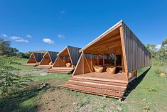 a group of wooden cabins sitting on top of a grass covered field next to trees