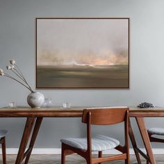 a painting hanging on the wall above a table with two chairs and a vase filled with flowers