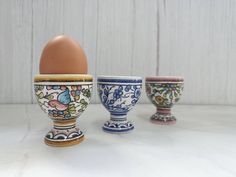 three egg cups with an egg in the middle one is painted blue and white, the other two are decorated red