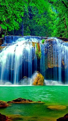 a large waterfall in the middle of a forest filled with green trees and water flowing down it's sides