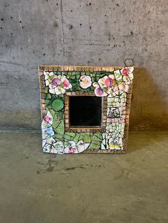 there is a small mirror made out of mosaic tiles with flowers on the outside and inside