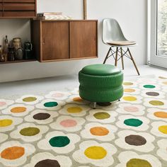 a green ottoman sitting on top of a rug in front of a wooden cabinet and window