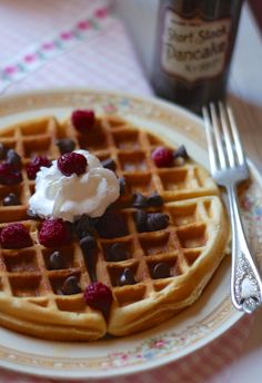 a plate topped with waffles covered in whipped cream and berries next to a bottle of syrup