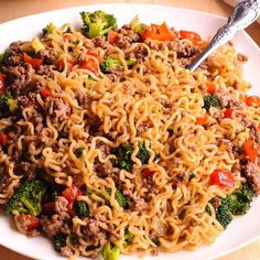 a white plate topped with noodles and meat next to broccoli on a wooden table