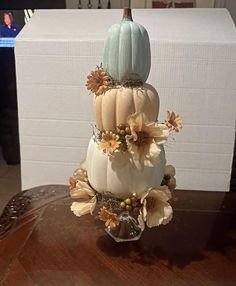 a three tiered cake decorated with white pumpkins and flowers on a wooden table