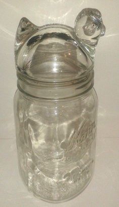 a clear glass jar with a cat head on the top and bottom, sitting on a white surface