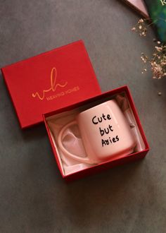 a coffee mug with writing on it sitting in a red box next to some flowers