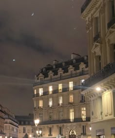 people walking down the street at night in an old european city with tall buildings on either side