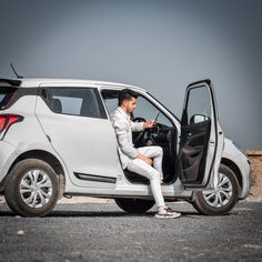 a man sitting in the driver's seat of a white car with his hand on the door handle