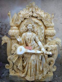 a statue of a woman sitting on top of a wooden chair in front of a wall