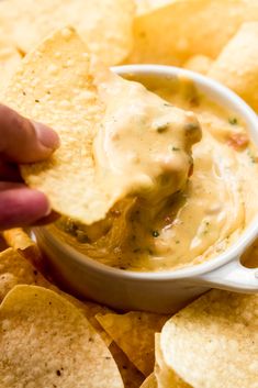 a hand dipping a tortilla chip into a bowl full of salsa and chips