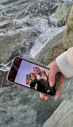 a person taking a photo with their cell phone by the water's edge,