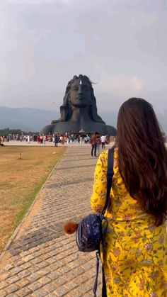 a woman in a yellow dress is looking at a large statue